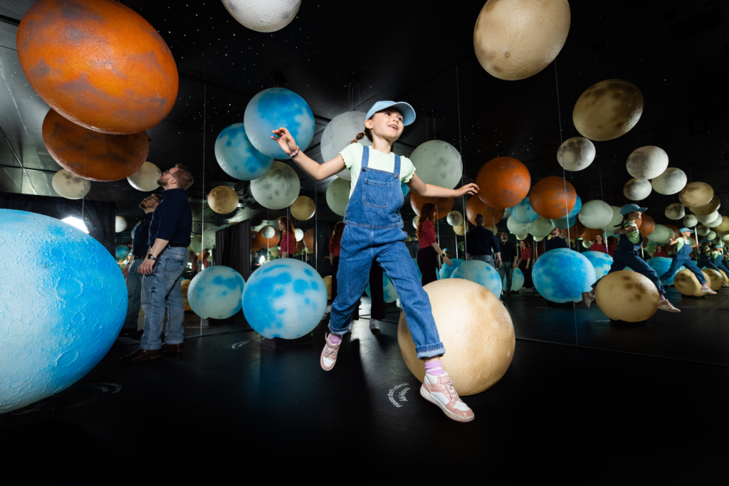 En person svävar i mörkret bland färgglada bollar.