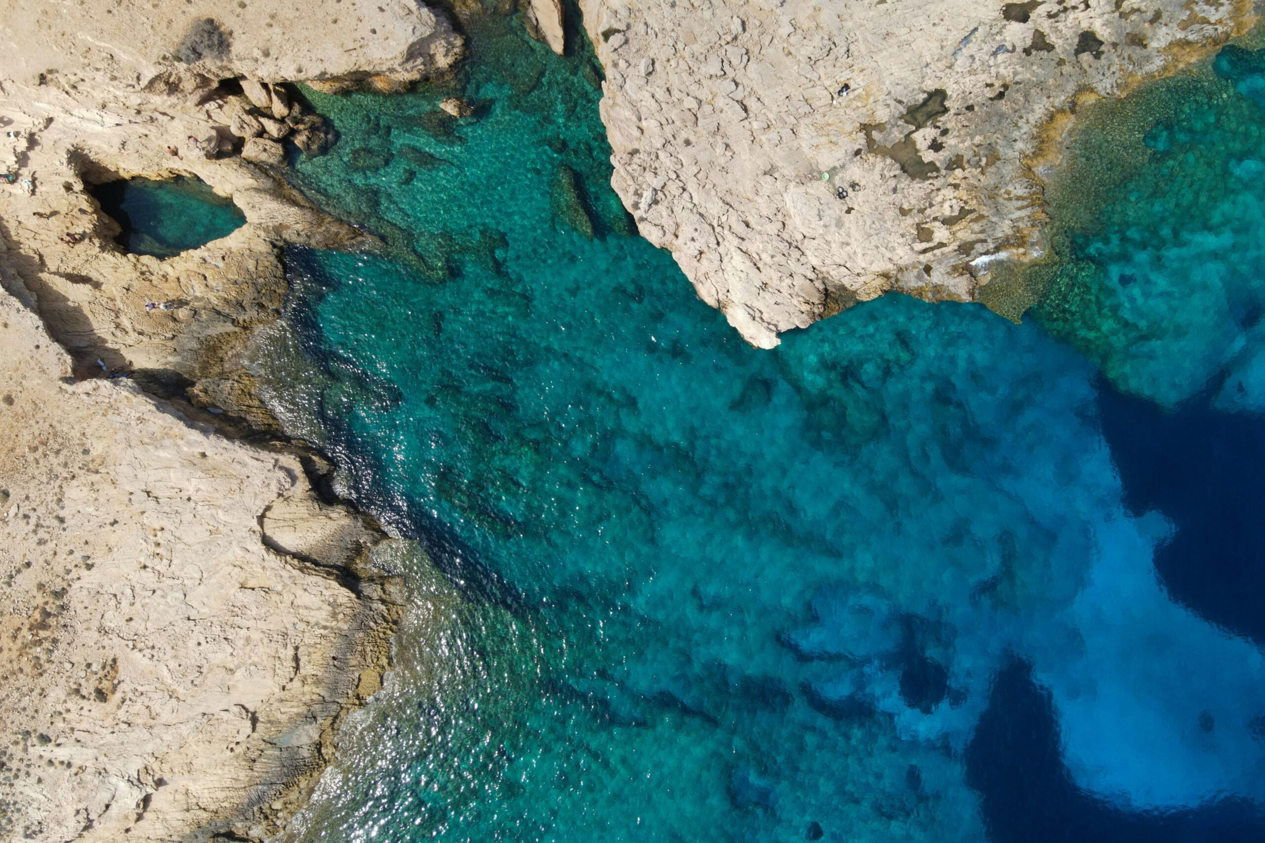 Drönarbild över kalkstensklippor och blått hav. 