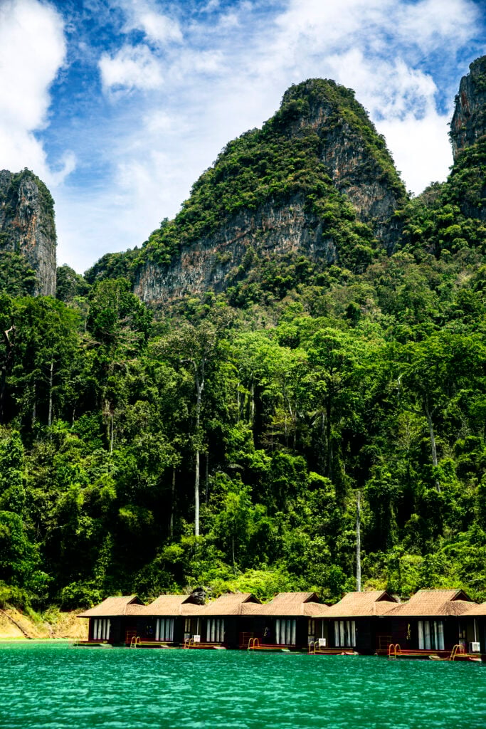 Flera små hus på flottar i vattnet framför djungeln.