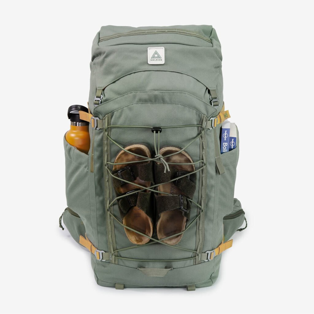 En grön ryggsäckar med ett par tofflor fastspända mitt på, en orange vattenflaska på sidan.