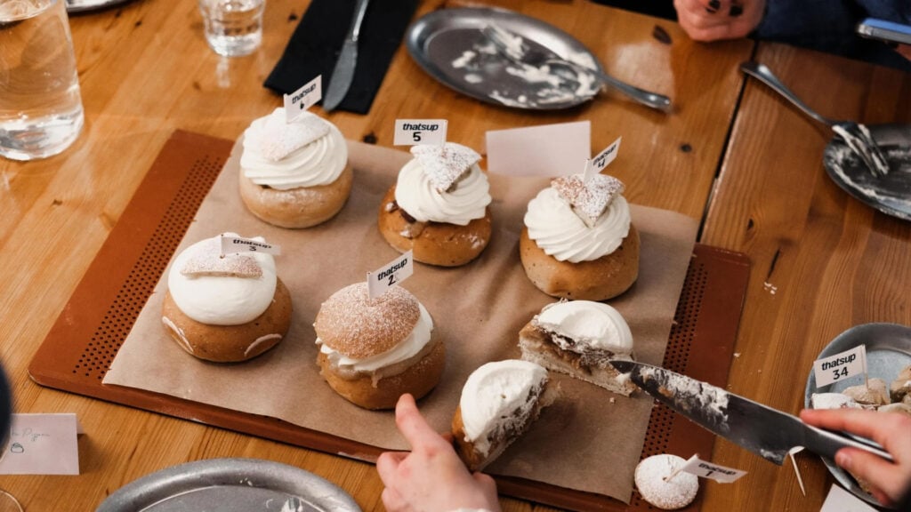 Sex semlor på en plåt, en kniv sticks fram och skär upp en semla.