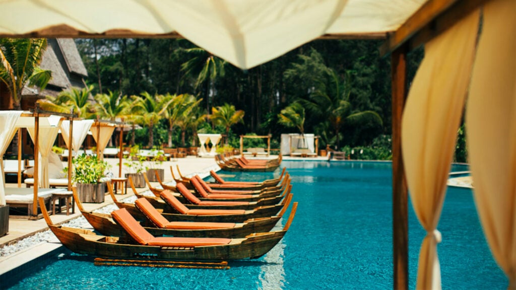 I en turkos pool flyter små båtar med solbäddar, gröna djungelberg.