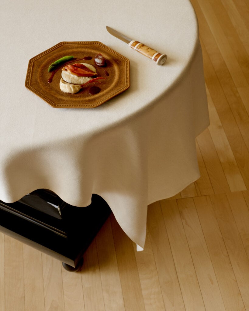 En rund bordskant sticker fram, med ett hexagonalt fat med mat och en grov jaktkniv. 