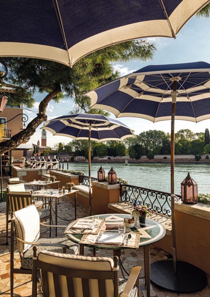 Dukade runda bord på en lyxig uteplats precis ovanför kanalen, blåvita parasoll med träskaft.