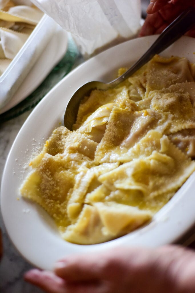 En tallrik med gul tortellini och en sked. Händer håller i tallriken. 