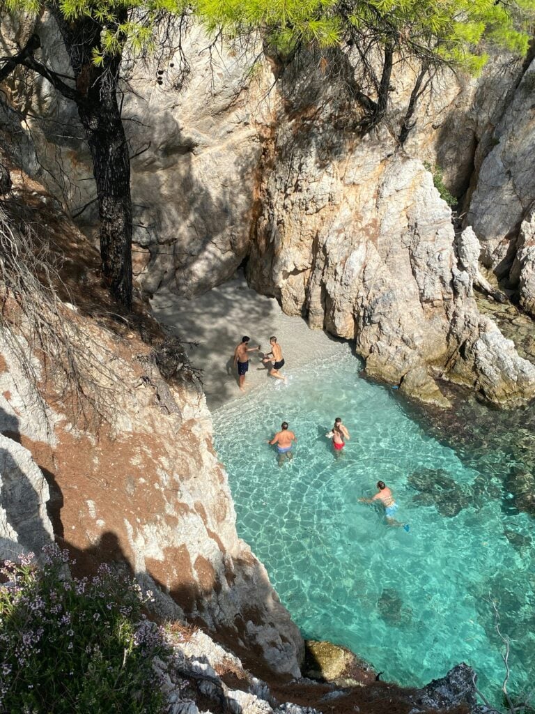 Fem personer badar på en liten strand, inklämd mellan dramatiska kalkstensklippor. Foto ovanifrån. 