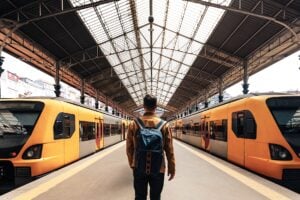 Man med ryggsäck på perrong mellan två gula tåg.