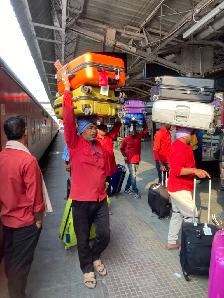 Bärare på järnvägsstation i Indien med väskor staplade på huvudet.