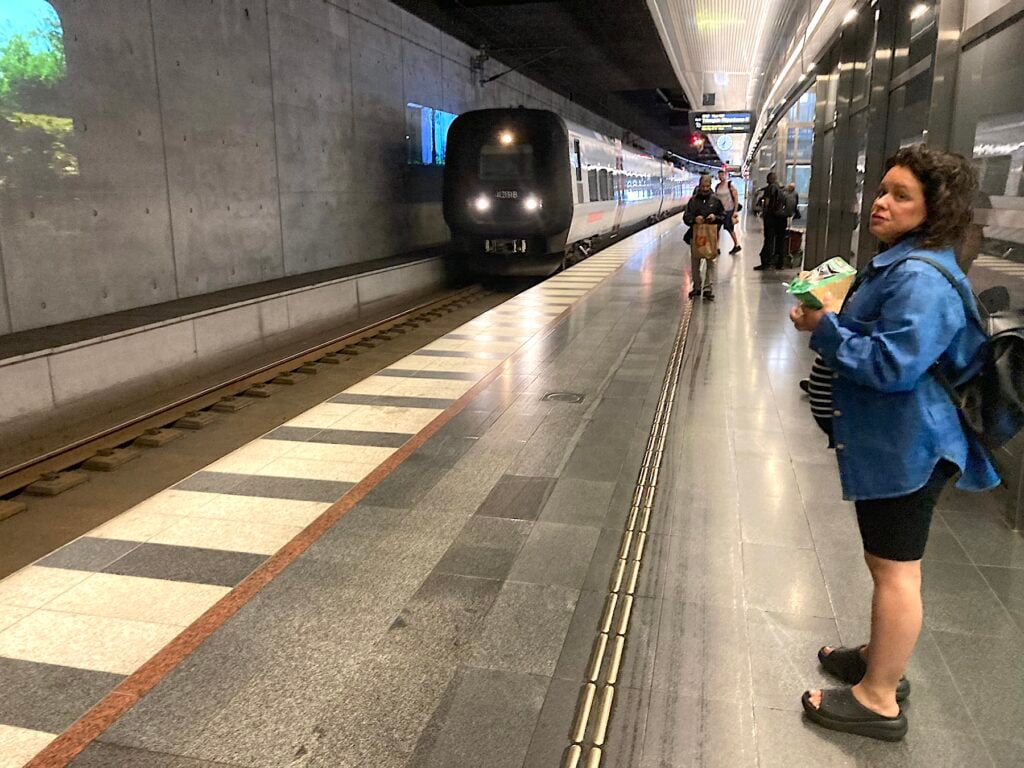 Kvinna på underjordisk perrong. Tåg på väg in.