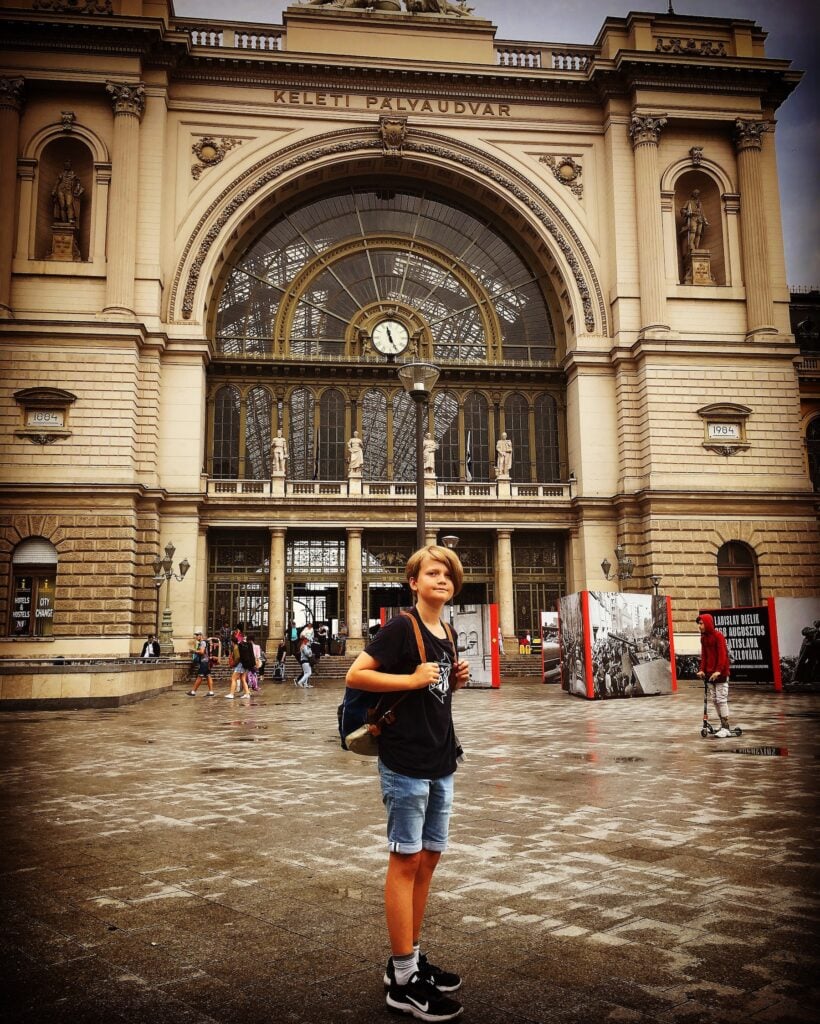 Pojke med ryggsäck framför järnvägsstation.