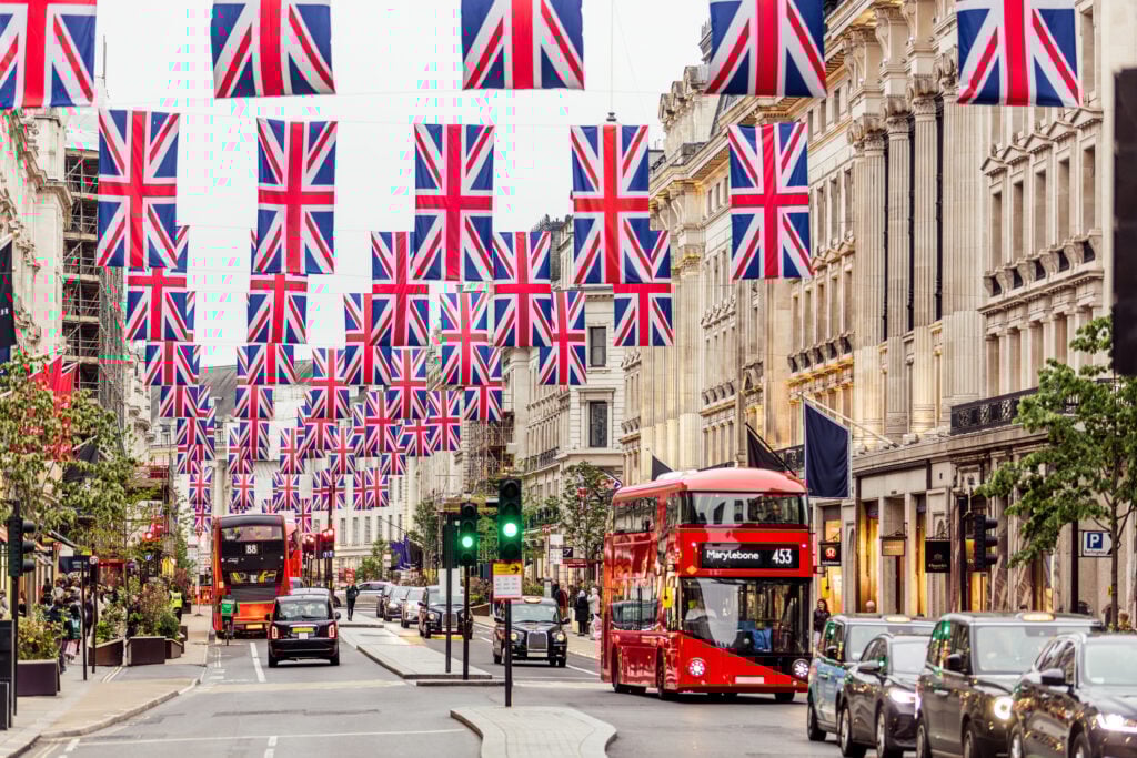 En gata i London är dekorerad med massor av brittiska flaggor, en modern dubbeldäckare trafikerar.