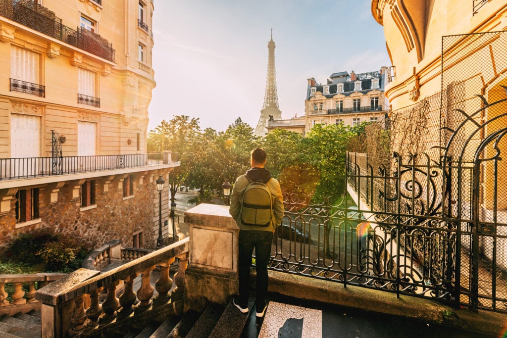 En man i ryggsäck står på en parkväg och tittar på Eiffeltornet i solnedgången. 