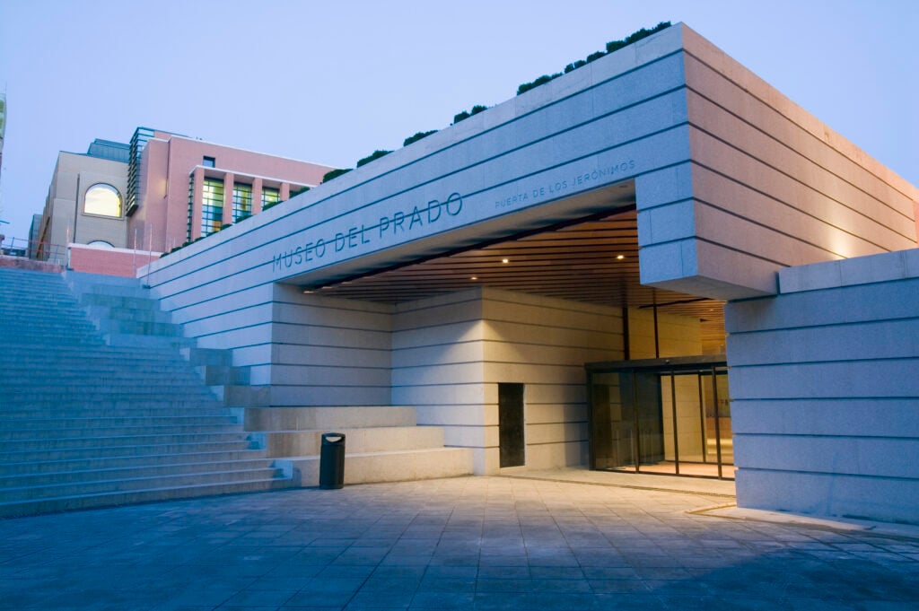 En grå, kantig modern byggnad syns bredvid en trappa i betong, skymning,