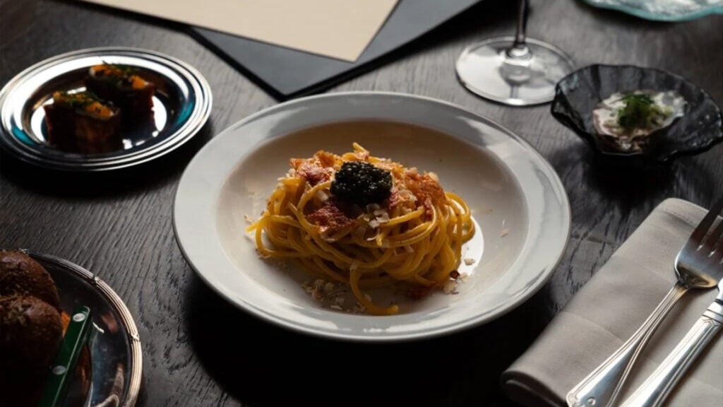 Ett svart träbord med en stor pastatallrik i mitten med svart kaviar. Bestick och småtallrikar vid sidan om.