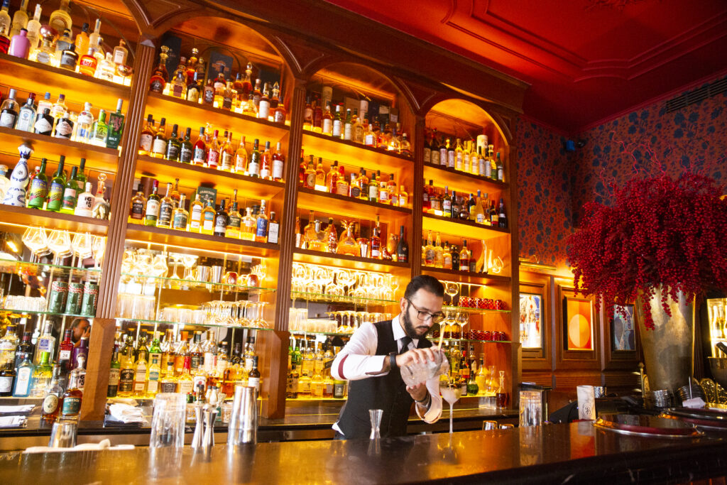 En bartender blandar en drink i ett högt glas, i en bar. 
