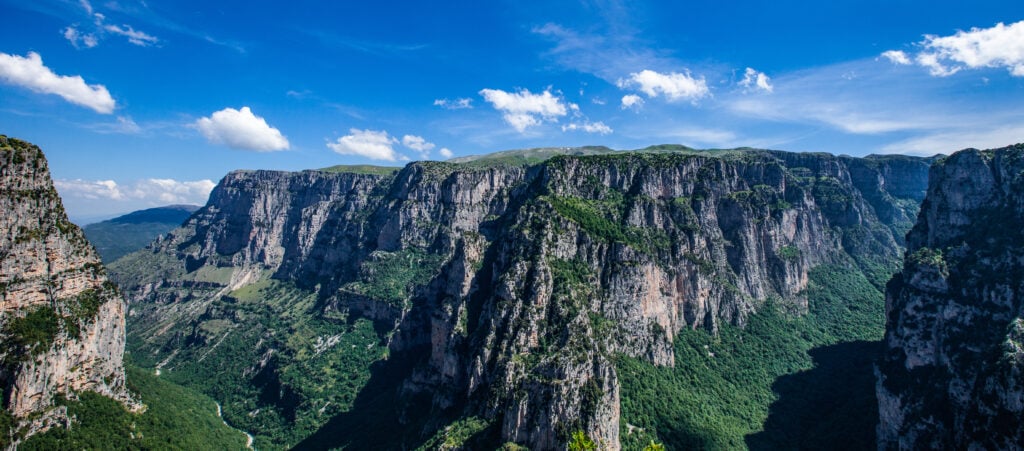Dramatiska gröna bergsravinter, med plattåer uppepå, sträcker sig under den blå himlen. 
