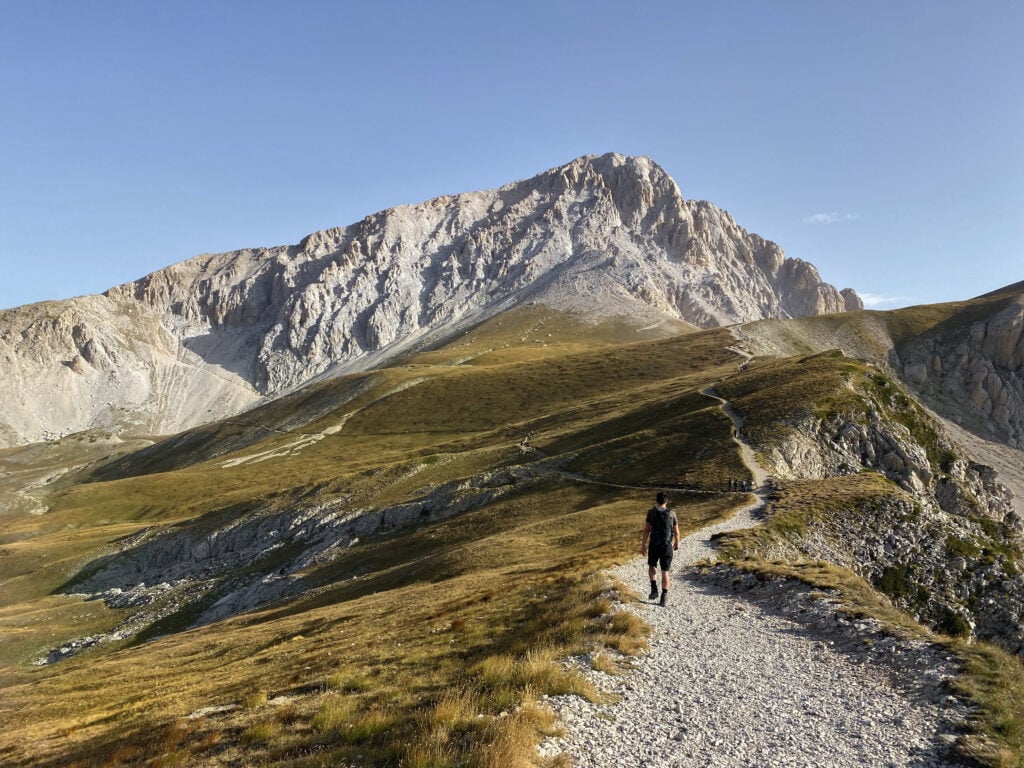 En vandrare på en grusväg som leder upp i ett dramatiskt berg. 
