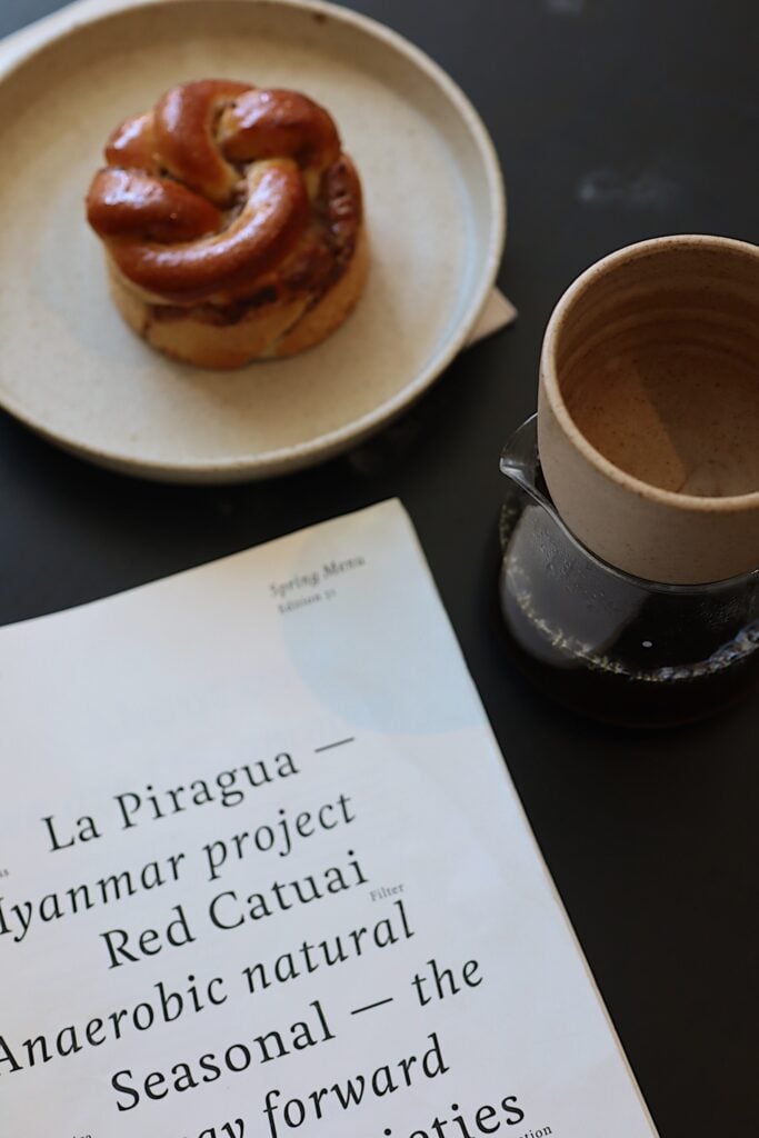 En meny, en tallrik med en bulle och en tom keramikkopp syns på bordet. 