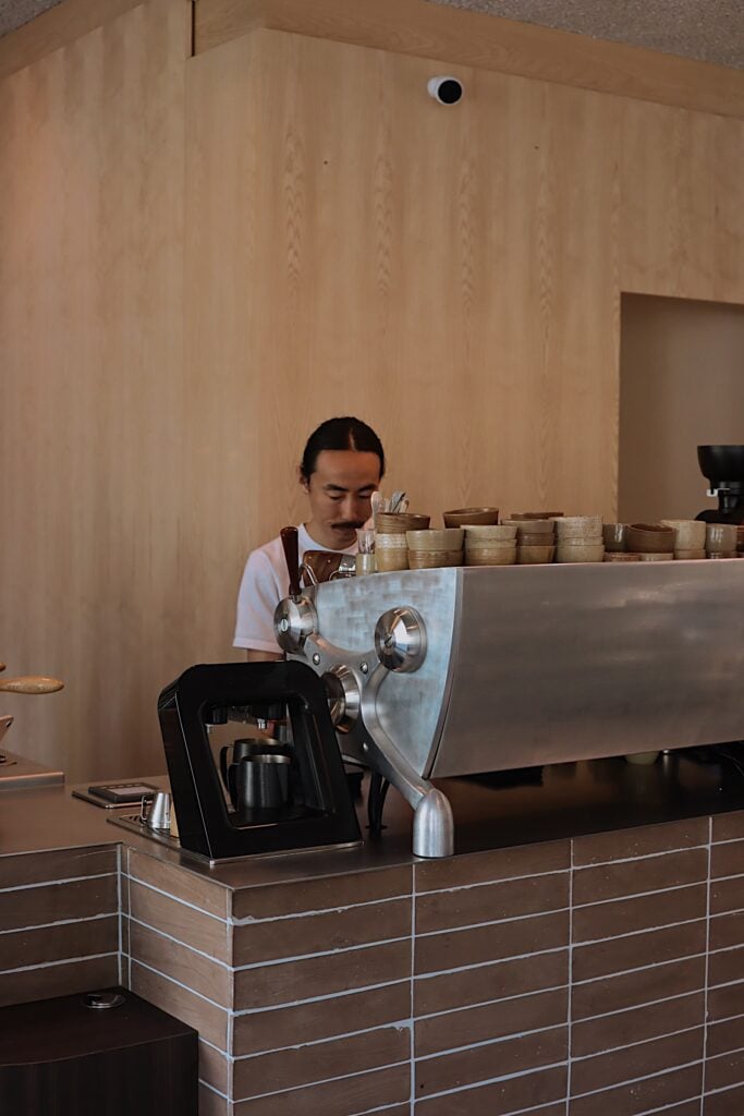 En man med svart hår står bakom en avancerad kaffedisk. 