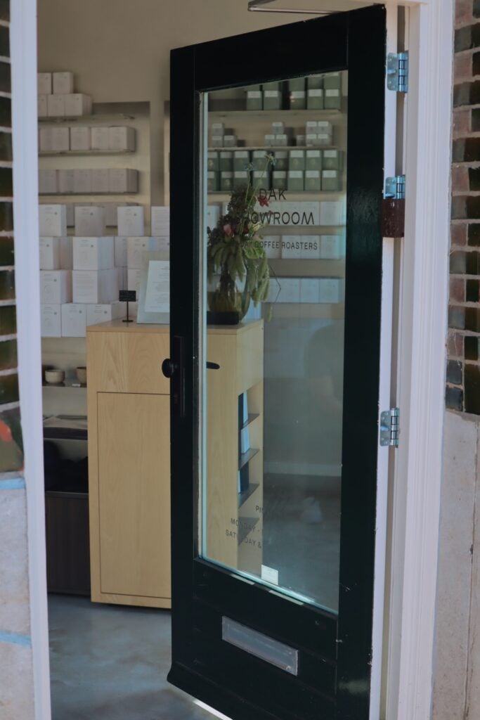 En svart dörr med glasfönster avslöjar ett rum med vita lådor och askar och en trädisk. 