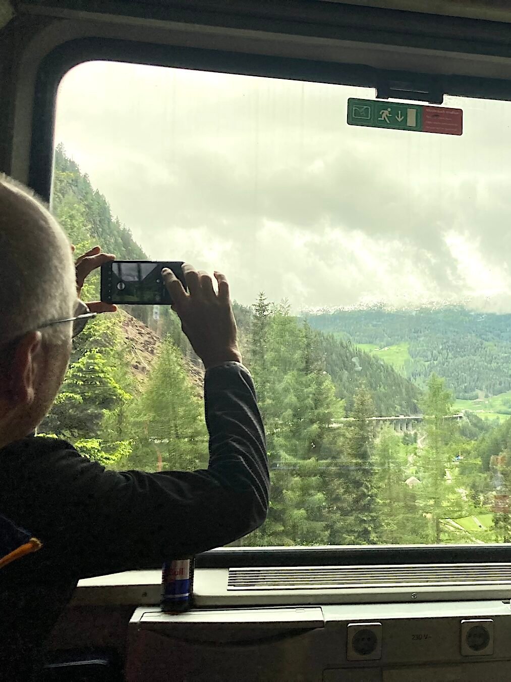 Två resenärer blickar ut genom tågfönster. Gröna berg utanför.