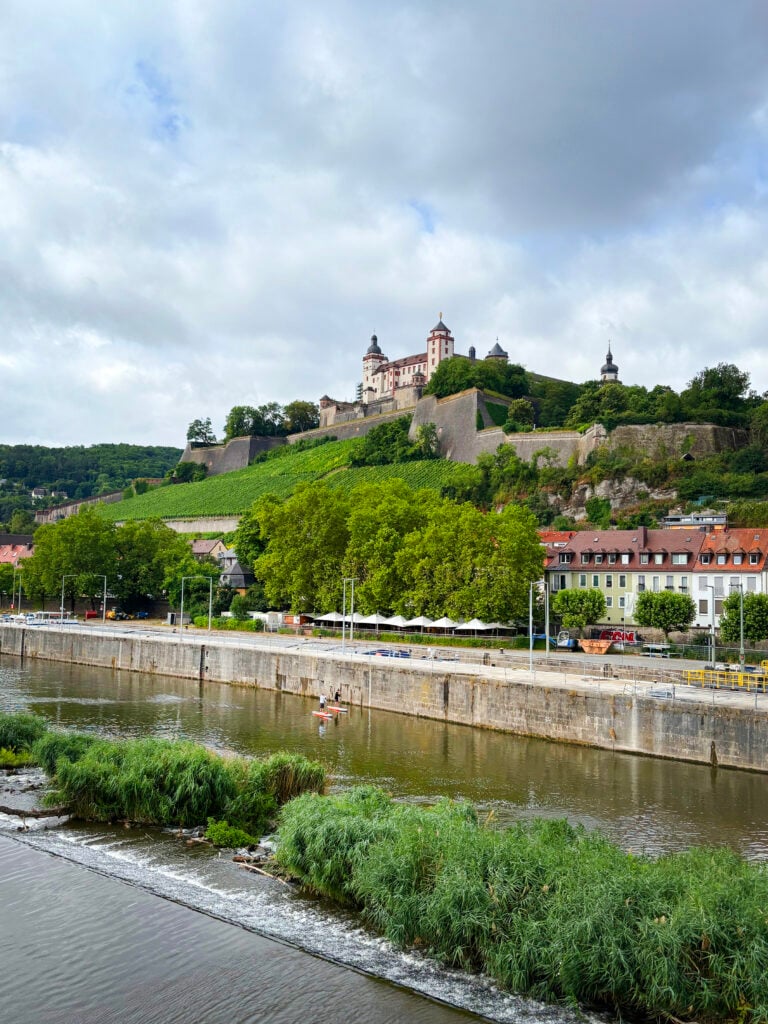 En fästning på ett grönt berg ovanför en stad med en kanal framför. 