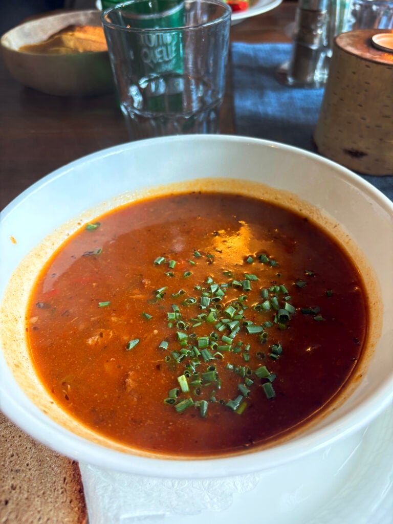 En vit tallrik med en brun gryta garnerad med något grönt. 