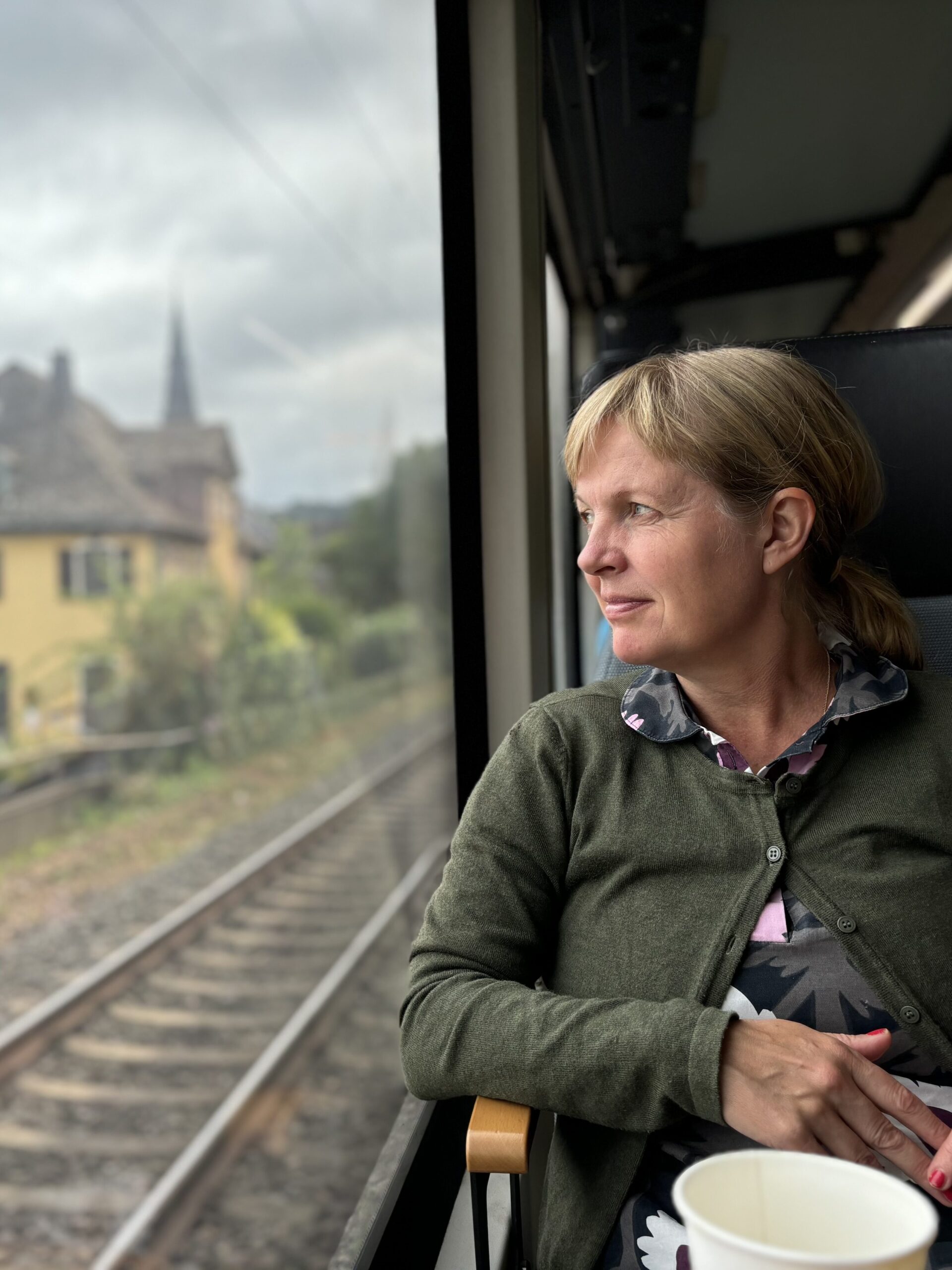 En kvinna sitter på ett tåg och tittar ut genom fönstret. Liten småstad passerar. 