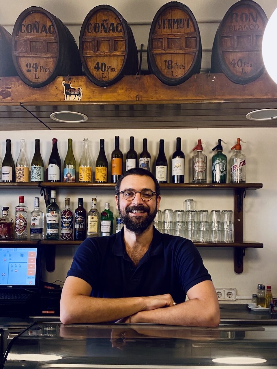 Bartender bakom bardisk med spritflaskor i bakgrunden.