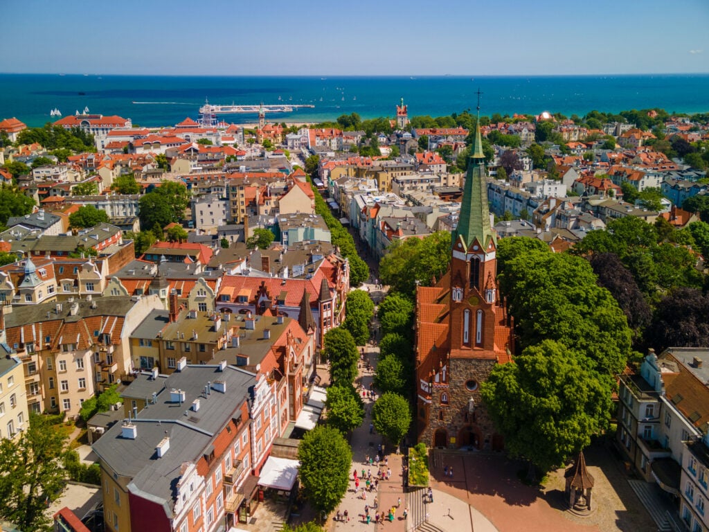 Flygvy över staden. Havet syns i bakgrunden. En spetsig kyrka sticker upp i mitten.