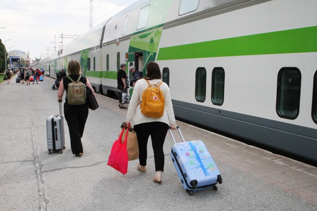Resenärer drar rullväskor på perrong intill tåg.