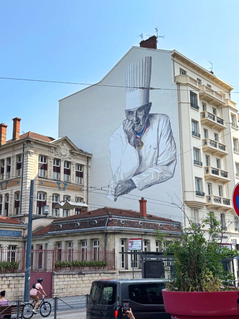 Paul Bocuse syns på en stor muralmålning över en vit husgavel.