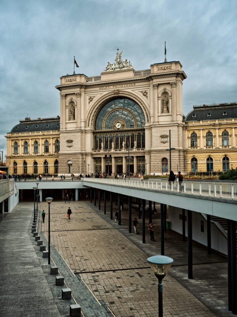 En pampig byggnad med stora kolonner reser sig över ett torg med gångbroar. 