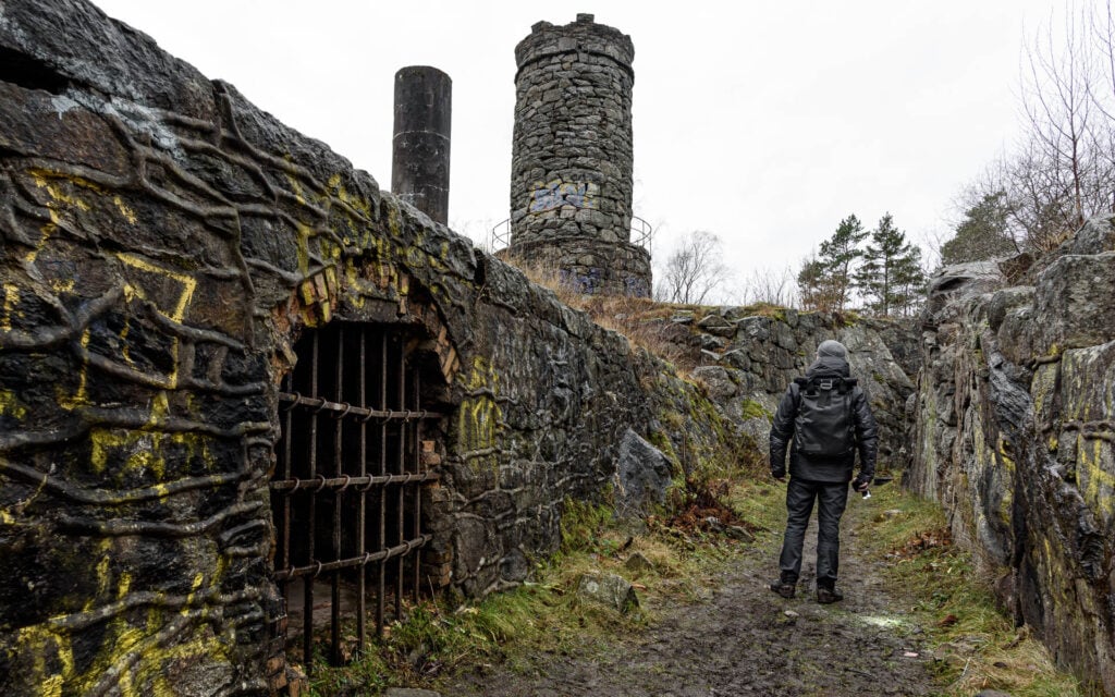 En man med svart ryggsäck går mellan urgamla murar, bredvid en gallrad fängelsehåla.