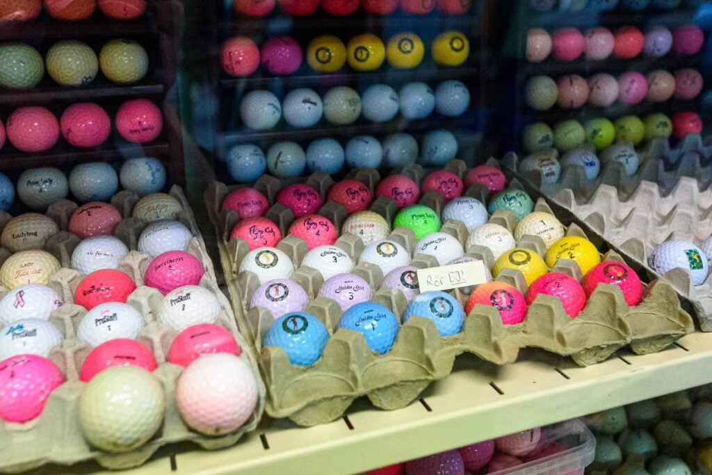 Färgglada golfbollar ligger upplagda på display, med en liten handskriven lapp "Rör EJ!"