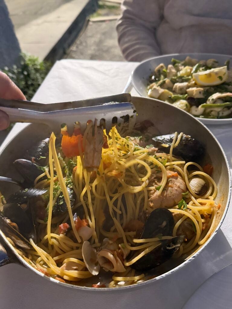 En solig tallrik med pasta med små musslor och en tång som griper i pastan. 