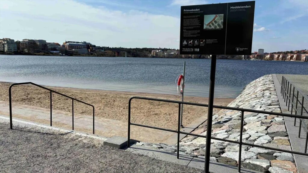 En stenpir sträcker sig ut i vattnet bredvid en badstrand.