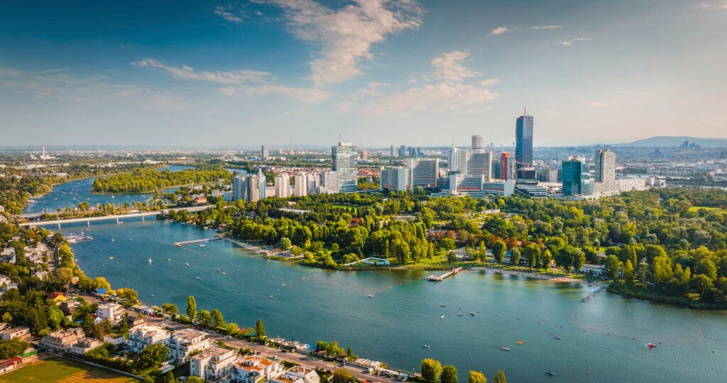 Aerial view of Vienna, Austria, showcasing the city's modern skyline including the skyscrapers of Donau City, with the Danube River and the lush greenery of the Danube Island (Donauinsel) in the foreground. Clear, sunny day. Vienna in Austria, Europe.
