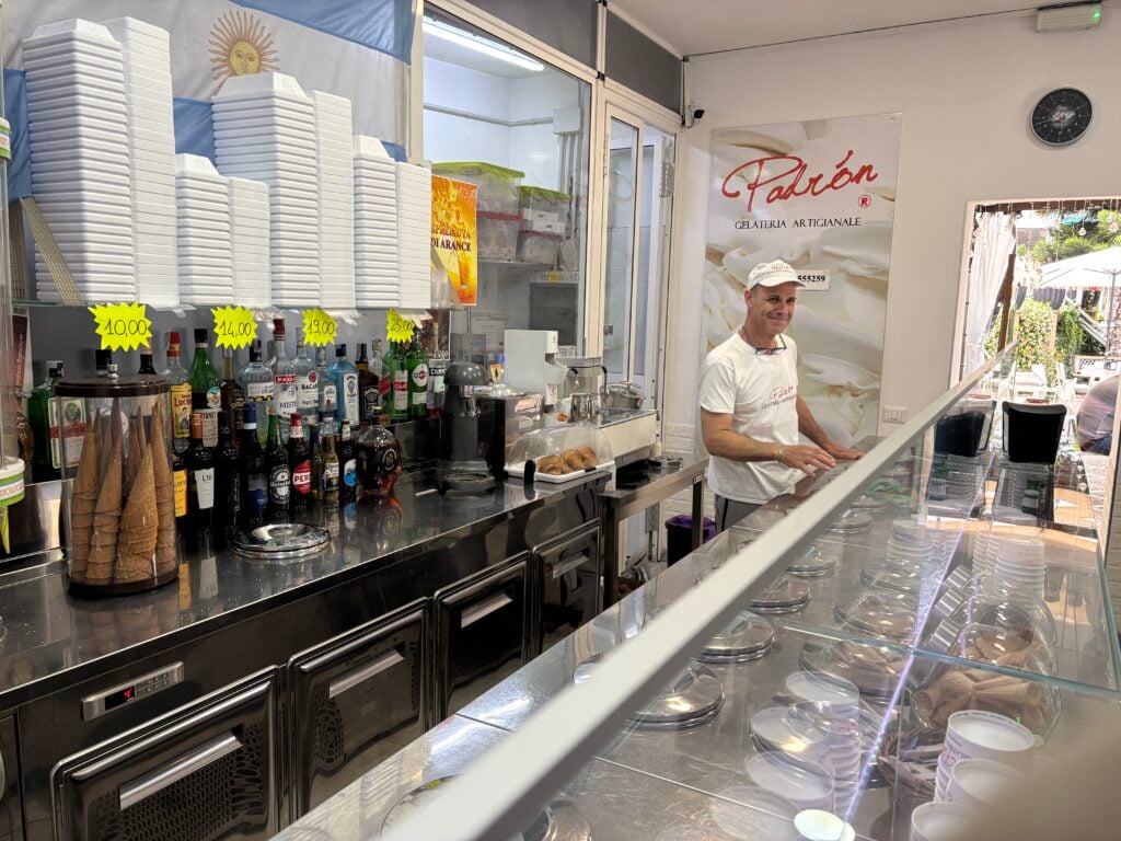 En man i vit keps står bakom en bänk i en glassbar. 
