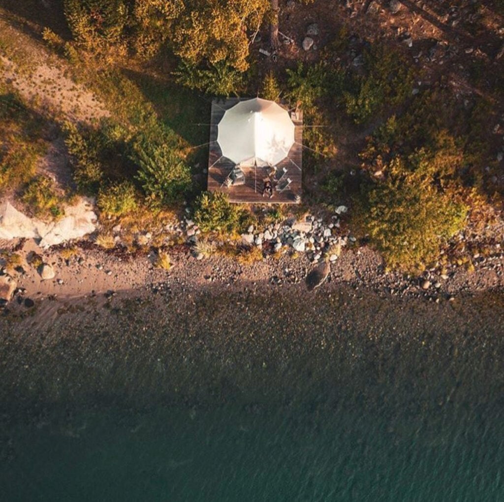 Drönarvy ovanför en strandkant och ett vitt tält. 