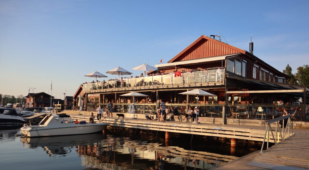 En krog bredvid vattnet, båtar förtöjda vid bryggan. Solnedgång.