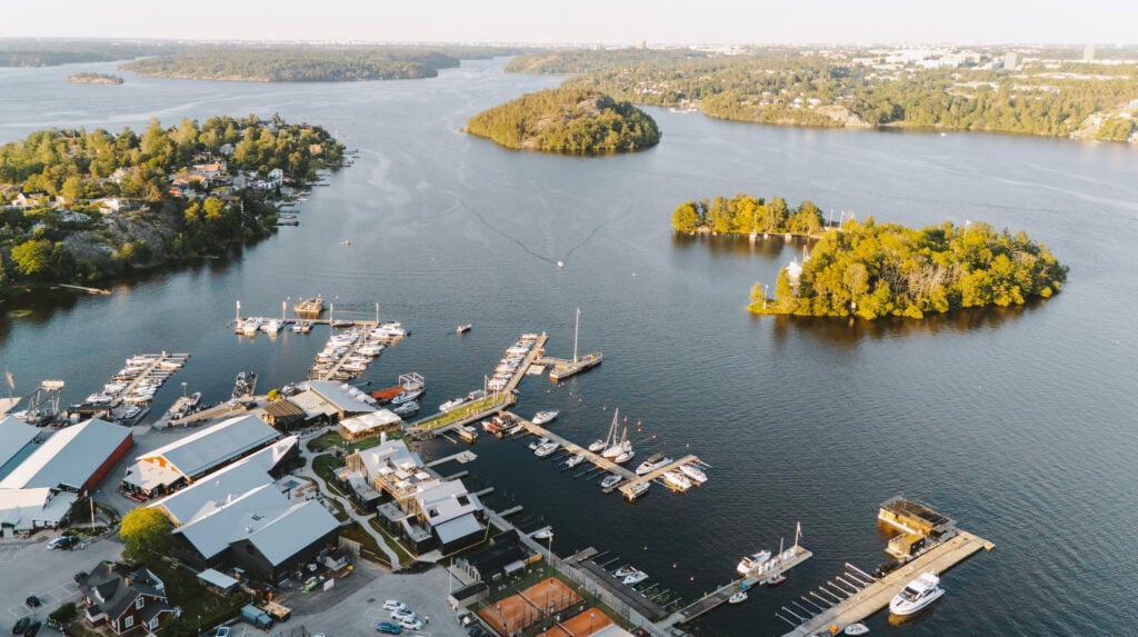 En drönarvy ovanför en byggnad vid en kajkant, hav, båtar, små gröna öar.