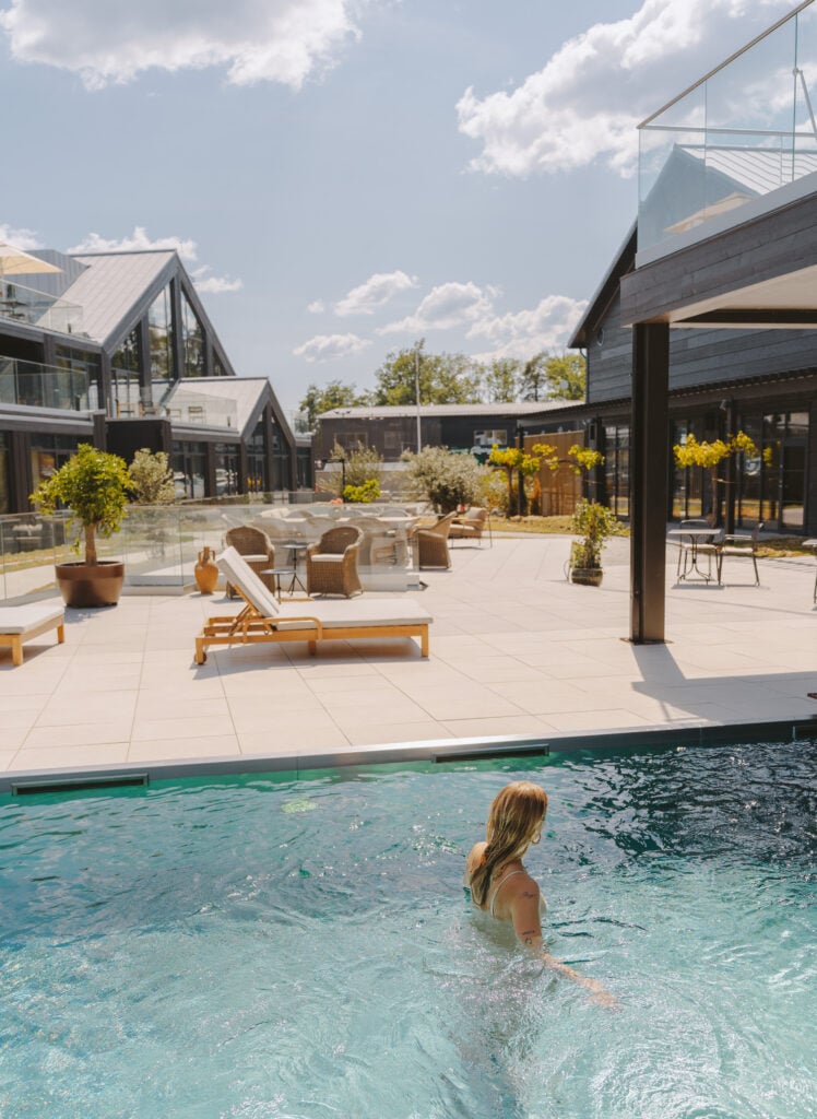 En person badar i en pool, bredvid ett stort pooldäck inramat av hotellbyggnad.