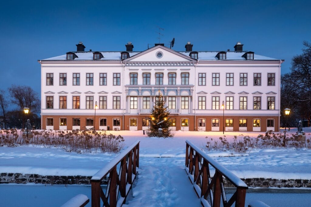 En stor vit herrgårdsbyggnad i ett mörkt snölanskap. 