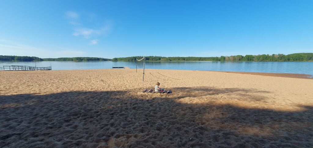 En strand med en liten pojke sitter på stranden bredvid vattnet.