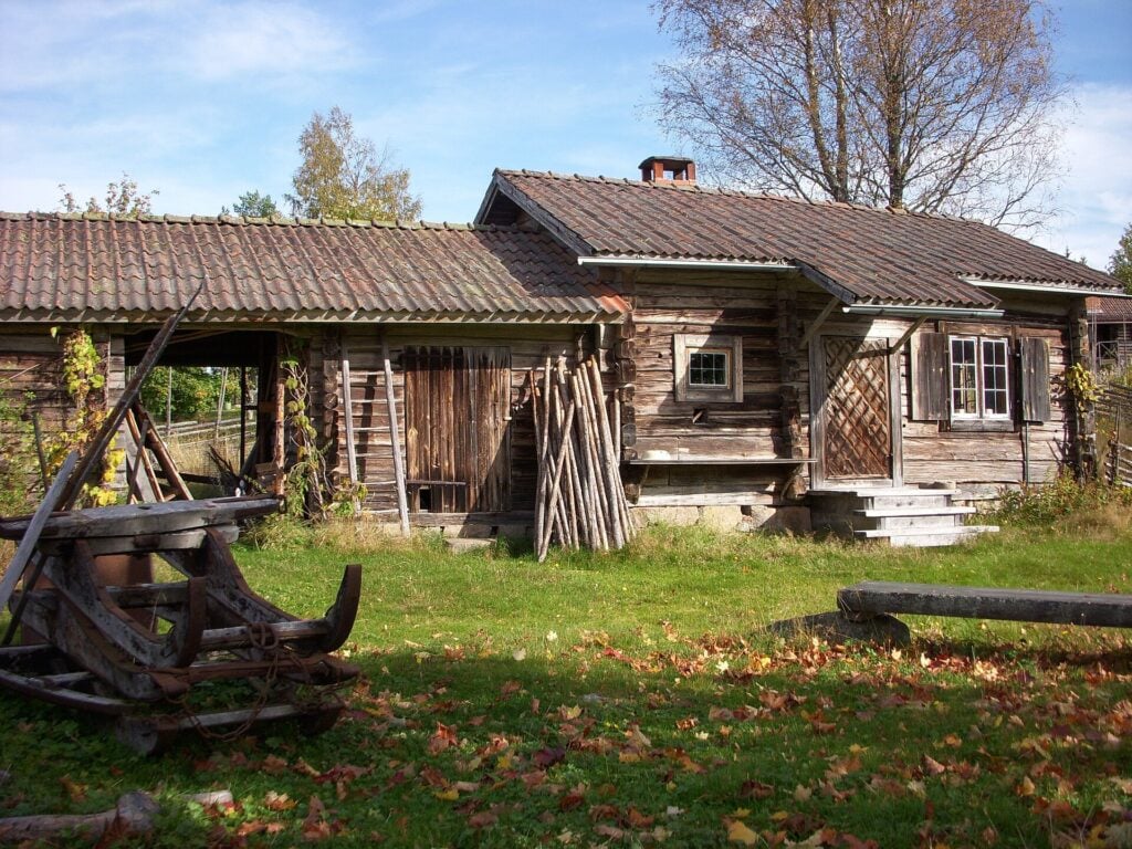 En väderbiten brun stuga framför en grön äng. 