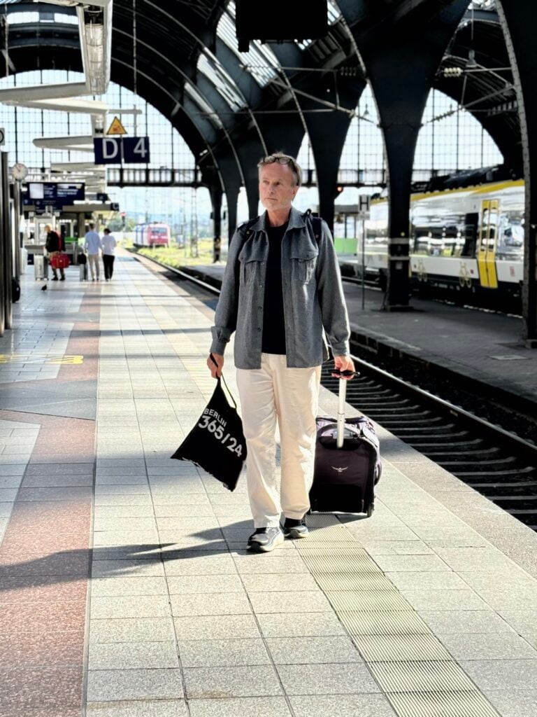 Man i grå jacka på tågperrong med rullväska i släptåg.