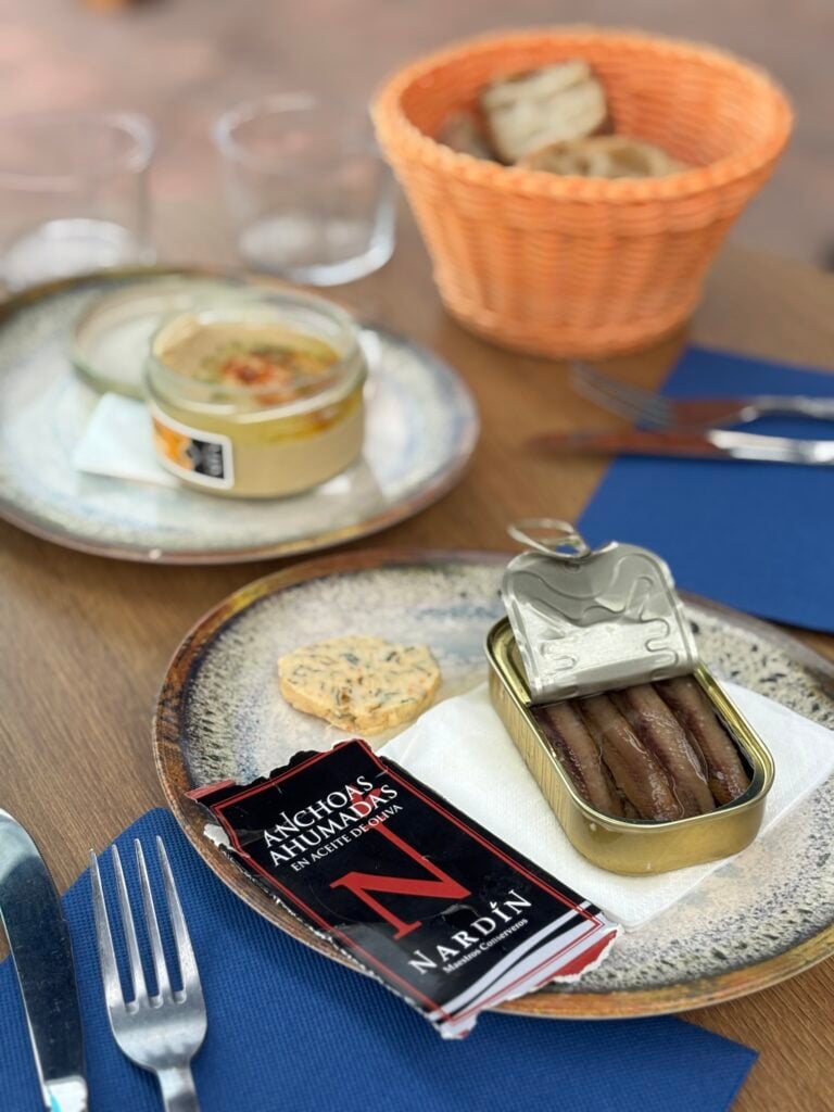 Sardiner i burk, hummus i burk och korg med bröd.