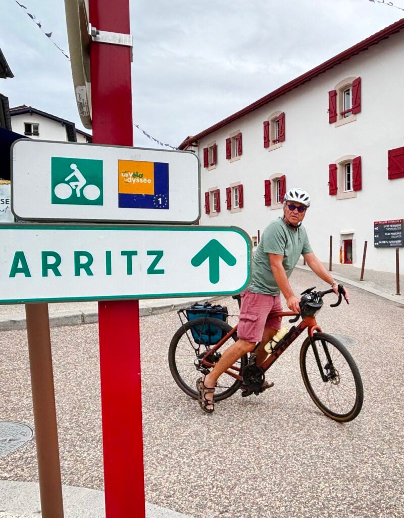 Man med hjälm på cykel i fransk by med skylt framför med texten Biarritz.