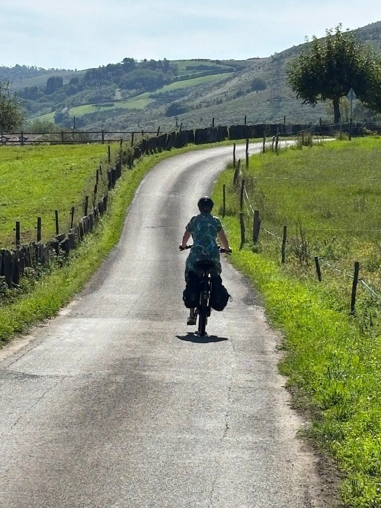 Kvinna på cykel i nutförslöpa på väg mellan gröna fält.
